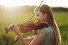 浪漫的女人宽松的头发玩小提琴日落光自然