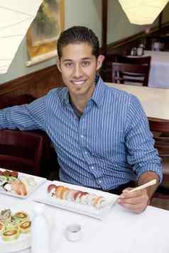 肖像英俊的年轻的男人。吃寿司日本餐厅