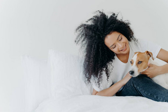 室内拍摄可爱的非洲式发型美国女孩休息床上觉醒狗享受时间宠物坐舒适的床上白色墙杰克罗素梗国家老板可爱的友谊