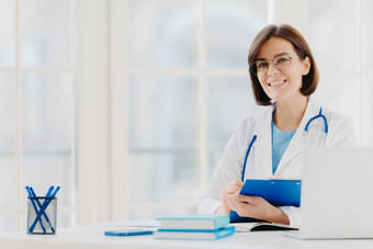 女医生写处方特殊的形式作品私人诊所穿白色医疗礼服准备好了病人提出了工作场所微笑医生医疗工人持有剪贴板