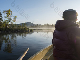 渔夫男人。划船船湖Sjabatjakjaure美丽的阳光明媚的早....阴霾雾瑞典拉普兰自然山桦木树云杉森林的客人天空背光