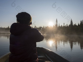 渔夫男人。划船船湖Sjabatjakjaure美丽的阳光明媚的早....阴霾雾瑞典拉普兰自然山桦木树云杉森林的客人天空背光