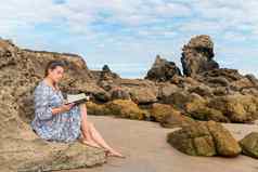 女人阅读书坐着岩石海滩