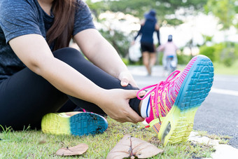 亚洲女人手持有脚踝运行路公园受伤锻炼概念