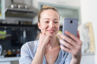 年轻的微笑快乐的很高兴女人在室内首页厨房社会媒体应用程序移动电话聊天住在猪圈里连接爱保持首页社会距离生活方式