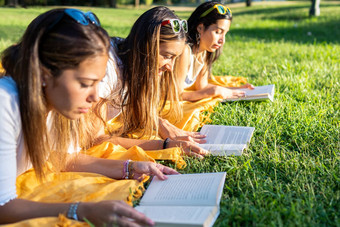 大学女学生说谎草公园早....阅读平装书书放松户外分享激情返回健康的习惯爱的自然