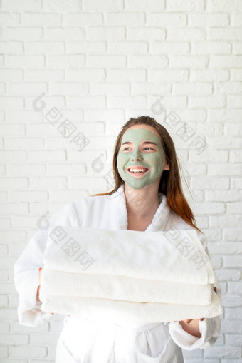 年轻的微笑高加索人女人脸面具穿浴袍持有桩白色浴毛巾