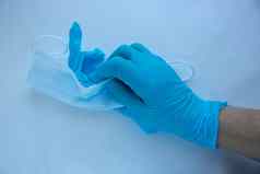 男人的手蓝色的乳胶手套持有面具白色背景保护手脸病毒