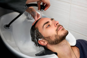 女人应用洗发水按摩头发客户男人。洗头发美沙龙理发师洗头发快乐高加索人的家伙享受服务理发店