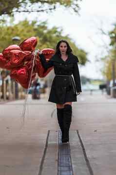 可爱的拉美裔浅黑肤色的女人模型庆祝情人节一天打红色的心气球