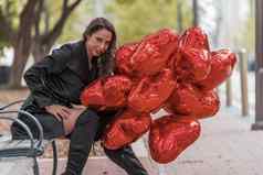 可爱的拉美裔浅黑肤色的女人模型庆祝情人节一天打红色的心气球