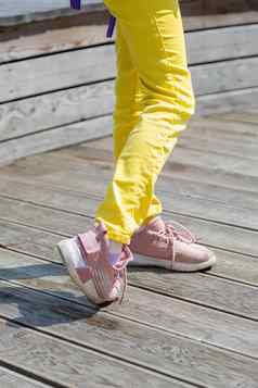 腿女孩黄色的牛仔裤粉红色的运动鞋夏天公园