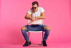 男人。坐在椅子白色t恤牛仔裤现代风格粉红色的孤立的背景