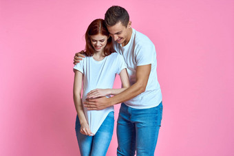 怀孕了妈妈快乐父亲粉红色的背景年轻的家庭等待婴儿