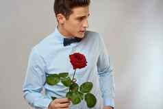 英俊的男人。红色的玫瑰蓝色的衬衫弓领带光背景裁剪视图
