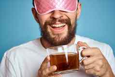 男人。粉红色的睡眠面具脸杯茶手裁剪视图特写镜头蓝色的背景