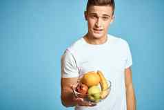 快乐男人。新鲜的水果手势手蓝色的背景白色t恤维生素香蕉橙子苹果