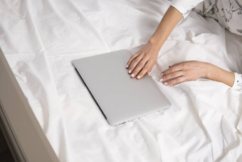 前视图女人坐着床上移动PC工作首页概念女孩工作移动PC床上白色床单放松工作过程保持首页