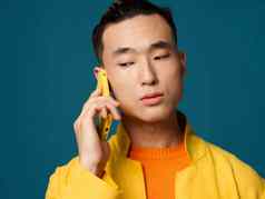 情感亚洲男人。蓝色的背景会说话的电话黄色的夹克
