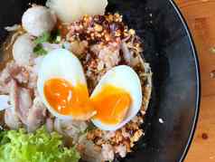 泰国辣的猪肉面条汤椰子牛奶蔬菜草本植物温泉tamago鸡蛋黑色的碗芝麻种子花生木表格视图