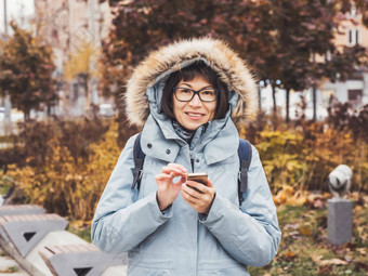 微笑女人光蓝色的温暖的夹克发短信智能手机在线沟通LTE无线网络无线细胞技术秋天季节小镇
