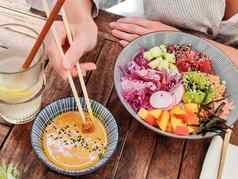 女人吃美味的色彩斑斓的健康的自然有机素食者夏威夷戳碗亚洲筷子乡村木表格健康的自然有机吃概念