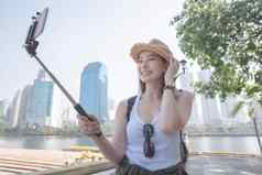 美丽的亚洲旅游女人采取自拍智能手机城市城市市中心