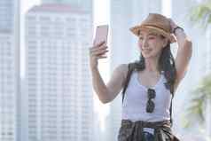 美丽的亚洲旅游女人采取自拍智能手机城市城市市中心