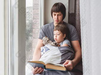 父亲读取书儿子舒适的家庭时间窗台上降雪蹒跚学步的男孩坐在毛茸茸的玩具封面毯子