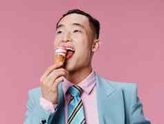 快乐亚洲男人。吃冰奶油粉红色的背景蓝色的经典西装
