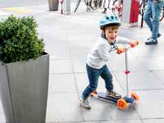 蹒跚学步的头盔骑踏板车停车很多停自行车城市车辆活跃的孩子们休闲活动男孩女孩