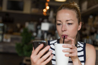 深思熟虑的女人阅读新闻移动电话喝着咖啡咖啡商店
