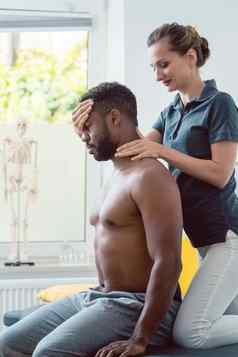 女人物理治疗师按摩年轻的黑色的男人。