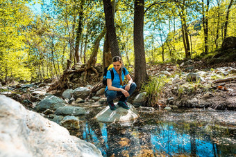 徒步旅行女人坐着石头中间溪通过森林