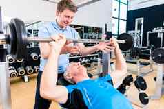 教练协助高级男人。提升杠铃健身房