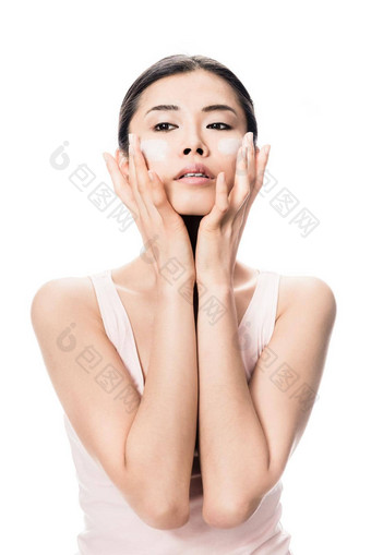 年轻的女人应用抗衰老保湿霜脸颊