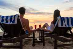 年轻的夫妇喝鸡尾酒海滩日落假期
