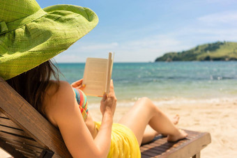 年轻的美丽的女人阅读书海滩阳光明媚的一天