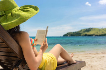 年轻的美丽的女人阅读书海滩阳光明媚的一天