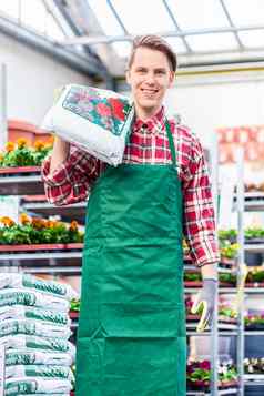 快乐的年轻的男人。携带袋盆栽土壤工作花商店