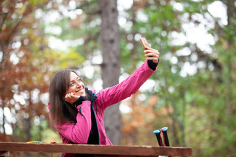 徒步旅行者女孩休息板凳上森林背包客粉红色的夹克采取自拍智能手机