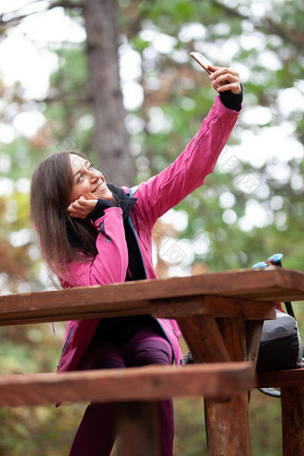 徒步旅行者女孩休息板凳上森林背包客粉红色的夹克采取<strong>自拍</strong>智能手机
