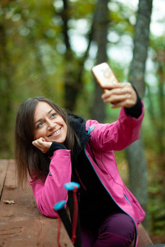 徒步旅行者女孩休息板凳上森林背包客粉红色的夹克采取<strong>自拍</strong>智能手机