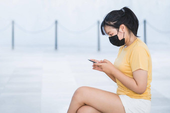 亚洲女人穿面部面具坐在浏览社会媒体更新科维德新闻移动电话正常的情况户外技术医疗概念