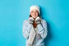 冬天假期概念可爱的红色头发的人女孩白色无檐小便帽手套微笑相机很高兴站蓝色的背景