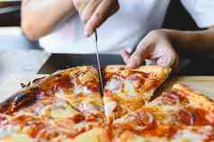 木火干酪披萨片手传统的夏威夷意大利蒜味腊肠披萨风味极佳的菜味道起源意大利餐厅木质的烤箱披萨人持有切割刀背景