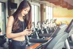亚洲女人聪明的电话锻炼强度培训健身健身房跑步机放松技术概念体育锻炼健康护理主题快乐舒适的情绪