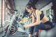 亚洲女人坐着健身球听音乐健身培训健身房聪明的电话放松体育运动锻炼培训概念技术娱乐主题