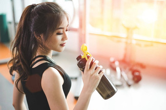 亚洲美丽的女人喝蛋白质摇喝水体育运动健身培训健身房体育人概念健身锻炼主题太阳耀斑效果
