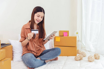 美亚洲女人平板电脑信贷卡开始小业务企业家锻造检查订单列表卧室年轻的快乐自由女人购物在线市场营销发送包裹